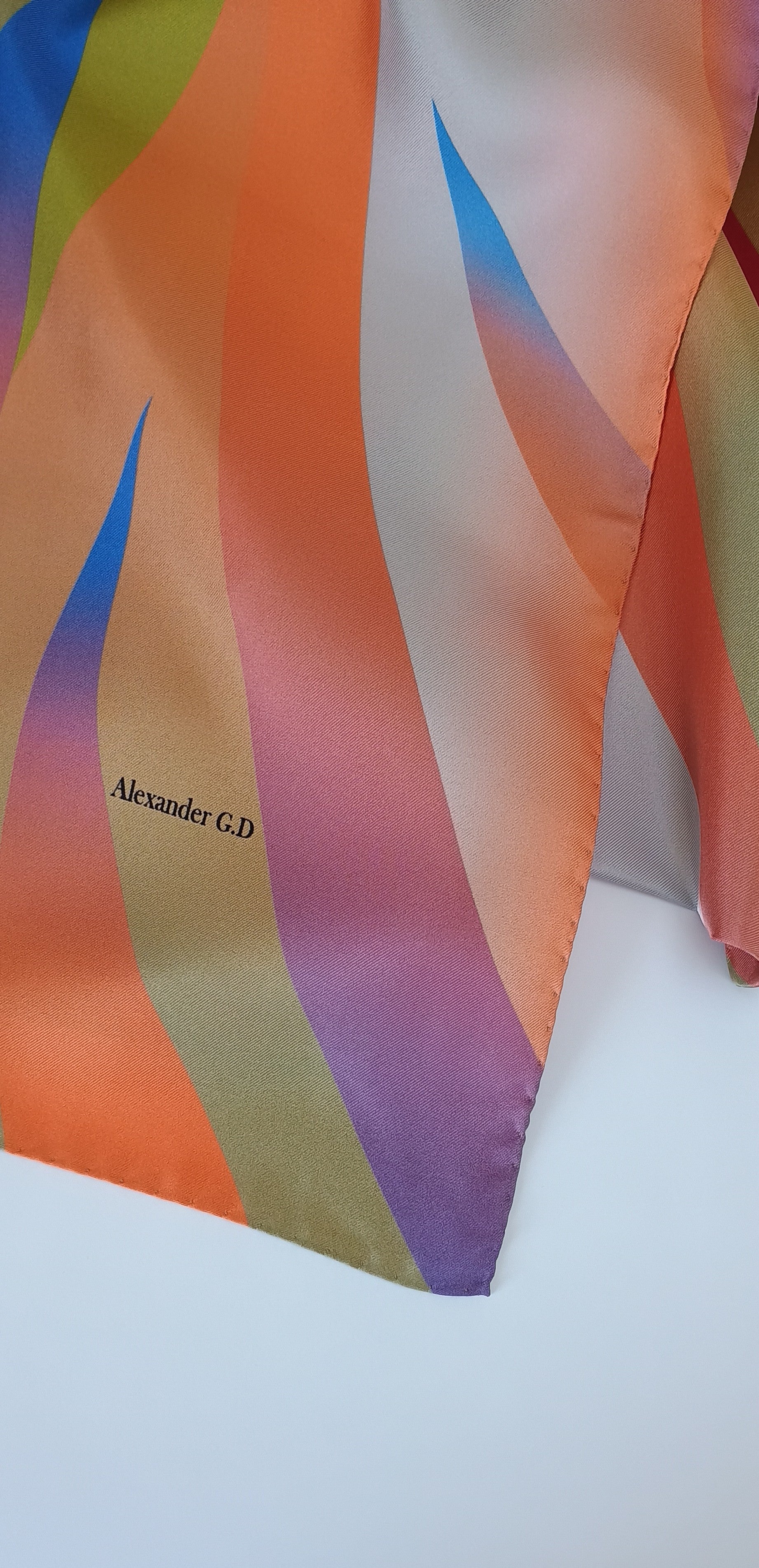 Colorful scarf with wavy pattern on a white background, featuring the brand 'Alexander G.D'.